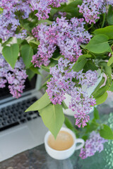 On the table are a bouquet of lilacs and a computer, a cup of coffee. Concept, work at home.