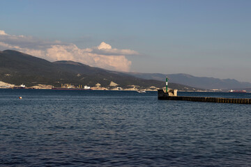 Fototapeta premium A windsurfer sails near the lighthouse against the backdrop of mountains in a sea bay on a clear day.