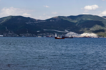 A tug is leading a cargo ship to the port against the backdrop of mountains in the afternoon.