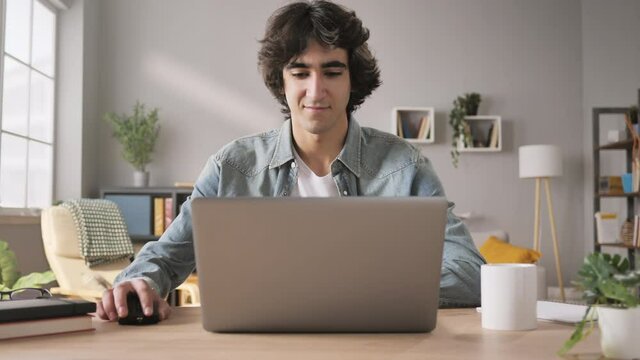 young satisfied man sits at his desk opens and starts using laptop,arab pleased male opening notebook computer looking at the screen reading news or email