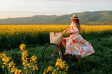 Girl with a red retro bicycle going along the yellow field of flowers.
