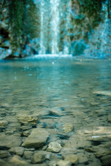 The rocky bottom of a mountain river against the backdrop of a small forest waterfall.