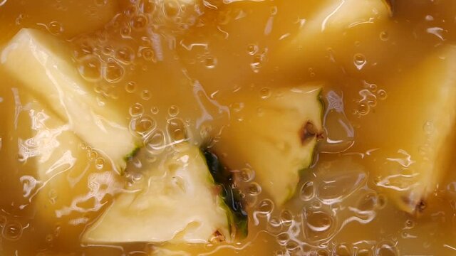 Pineapple slices falling and splashing into pineapple juice, slow motion, close up view. Juicy fresh summer fruits.