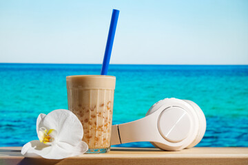Relaxing, summer resort concept. Glass of bubble tea, headphones and flower, blue sea on background. 