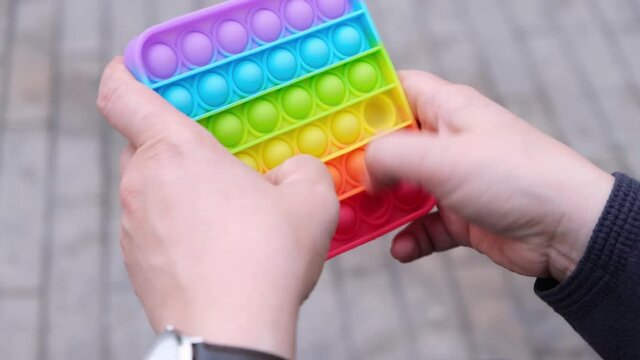 Female hands hold rainbow Square Fidget Toy Pop-it. Color silicone anti-stress toy pop it. Using popular relaxing square shape silicone stress relief toy.