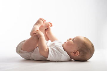 baby lies on his back, holding his legs, on a white background - 437606310