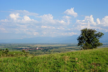 Obraz premium Countryside landscape in Tara Fagarasului depression in Transylvania, Romania viewed from a hill, with villages, fields and mountains and white clouds on blue sky 