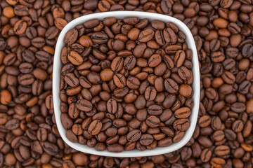 White glass bowl of coffee beans on the coffee background