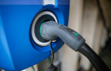 Shallow depth of field (selective focus) image with an electric car charging cable and plug at a charging station.