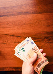 Hand holds stack of fifty euro banknotes wooden table background. Wages and minimum salary in...