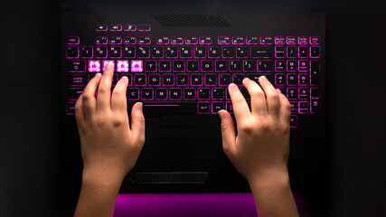 Hands typing on black gamer laptop with backlit keyboard © Yazmin DLC