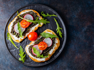 Healthy food. Avocado toasts with avocado, cream cheese and radish. Toasts with avocado, arugula and cherry tomatoes on a dark background. Copy space. Top view