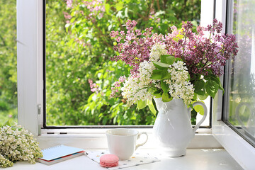 Home interior with decor elements, beautiful spring lilac branches in a vase on a sunny window, abstract flower arrangement, still life with place for text, floral birthday card, wedding,