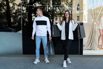 Fashionable guy and girl after shopping. Happy couple with shopping bags next to showcase. Black friday, shop discounts.