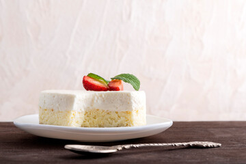 Cheesecake cake on white plate next to teaspoon. Side view