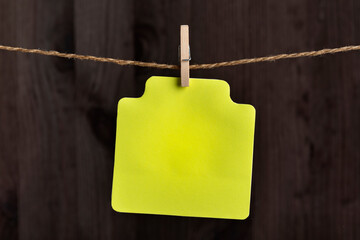 Blank yellow paper card hang with clothespin on rope. Copy space. Place for your text. Wooden background.