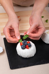 Hands of confectioner decorate cake. Fresh berries, mint and white meringue.
