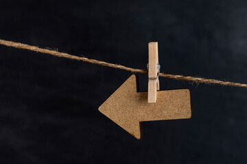 Arrow pointer hanging with clothespin on rope string peg, black background. Wooden arrow pointer