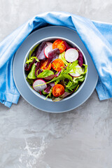 Healthy vegetable salad with cherry tomatoes, radish and mix salad. Vegan salad with mix of greens on gray background. Paleo diet concept. Copy space. Top view