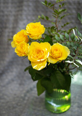 Beautiful yellow roses in a green vase stand on a blanket. Surprise and holiday concept.
