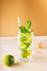 Mojito cocktail in a tall glass. Summer cocktail, lime and wooden juicer on a golden background. Refreshing drink with lime, mint and ice