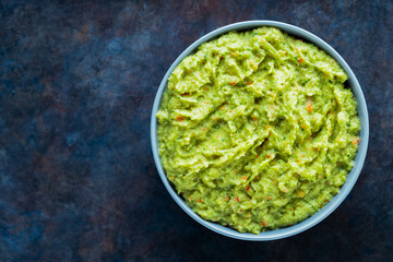 Guacamole in a gray bowl on a dark background. Bowl of avocado guacamole sauce with fresh ingredients. Copy space. Top view - obrazy, fototapety, plakaty