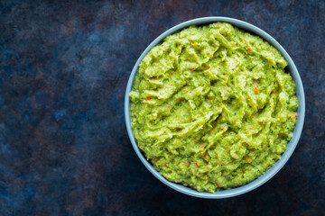 Guacamole in a gray bowl on a dark background. Bowl of avocado guacamole sauce with fresh ingredients. Copy space. Top view