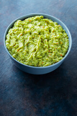 Guacamole in a gray bowl on a dark background. Bowl of avocado guacamole sauce with fresh ingredients. Copy space. Top view