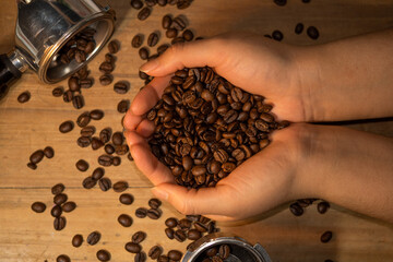 Hands holding coffee beans on a wooden table next to espresso portafilter