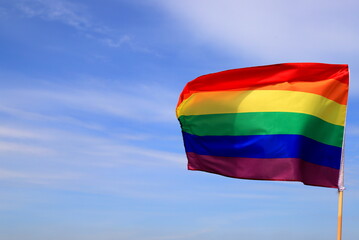 Waving gay pride rainbow flag in blue summer sky. Bright flag of the LGBT community for lesbian, gay, bisexual, transgender.