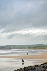 Fototapeta na wymiar People walking on a sandy beach, cloudy sky. Lahinch town, county Clare, Ireland