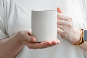 Fototapeta na wymiar Female hands holding big beige mug with empty surface for design.