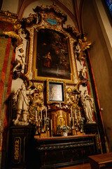 Fototapeta na wymiar Decorative interior of church St. Henry and St. Kunhuty, gilded ornamented baroque altar, white flowers, tall candles, marble statues, wood carved benches, Prague, Czech Republic