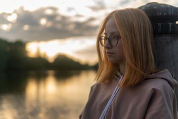 Portrait of a teenage girl with red hair at sunset on the shore of the lake