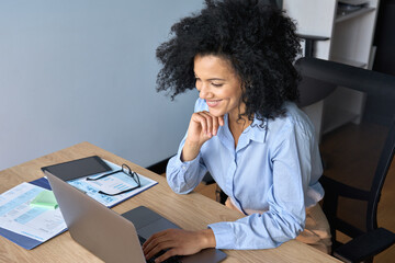 Happy smiling African American businesswoman executive manager sitting at desk working typing on...