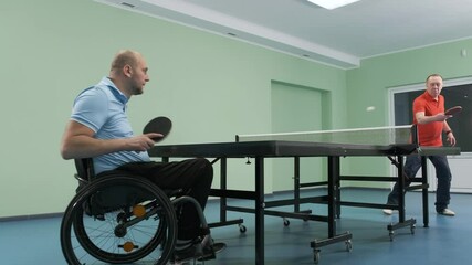 A man in a wheelchair plays ping pong. People with disabilities play table tennis. Rehabilitation of the disabled. Sport.