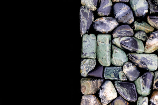 Kambaba jasper heap jewel stones texture on half black background. Place for text.