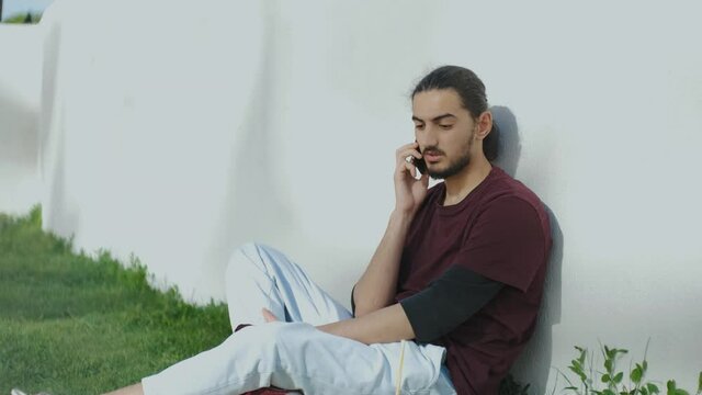 portrait of young attractive arab man sitting on the grass and talking on the phone. Man in park