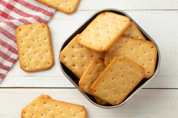 Cracker cookies in a stainless steel bowl with tablecloth on white wooden table background.