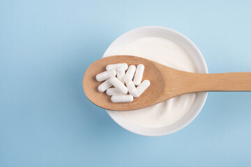 Capsules probiotic on a wooden spoon and bowl with homemade yogurt on light blue background....