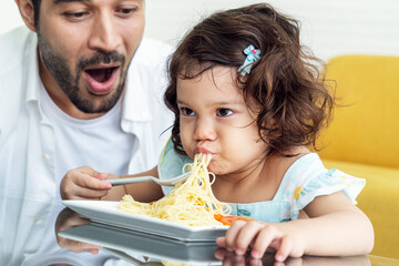 A father is thrilled to see his curly-haired daughter eat spaghetti, wanting to be happy at home 