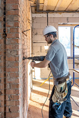 Handyman in the process of drilling a wall with a perforator.