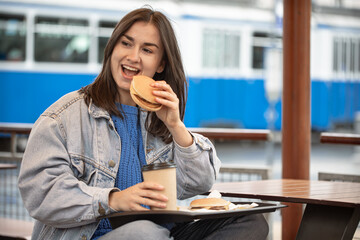 Fototapeta premium Street portrait of cheerful young woman eating fast food.