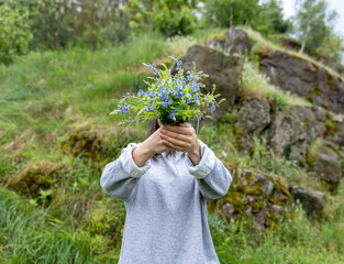 The girl covers her face with a bouquet of wild forest flowers.