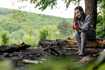 Girl with a cup of hot drink near the fire in nature.
