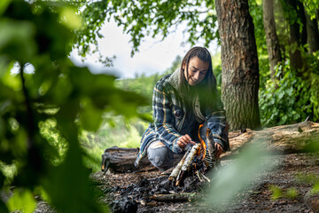 Fototapeta premium A cheerful girl in a hike in the forest makes a bonfire.