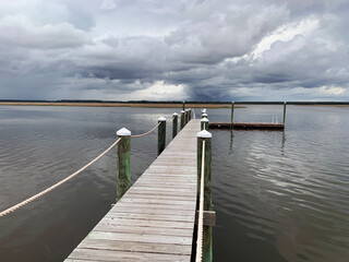 Obraz premium Wooden dock with ropes on stormy cloudy day over water on salt marsh