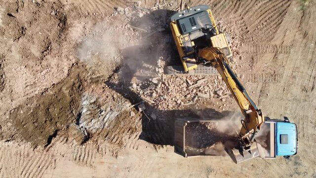 Excavator working on a construction site. Yellow excavator  loading a truck on field. Building demolition. Digger cleaning ruins. 