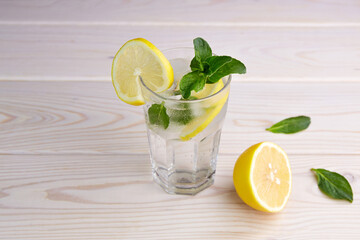 A glass with lemonade or mojito on wooden background. Fresh cold refreshing summer cocktail with lemon, mint and ice.