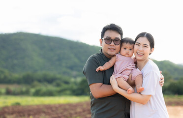 Happy asian family father mother child daughter on nature background . Parents hug little baby in arm standing outdoor with sunny day.